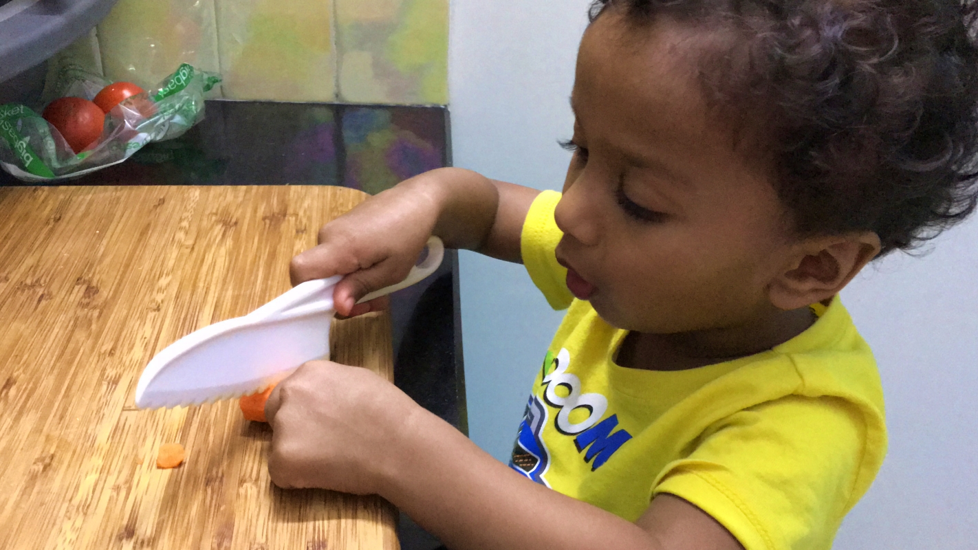 Toddler using a plastic knife to chop a