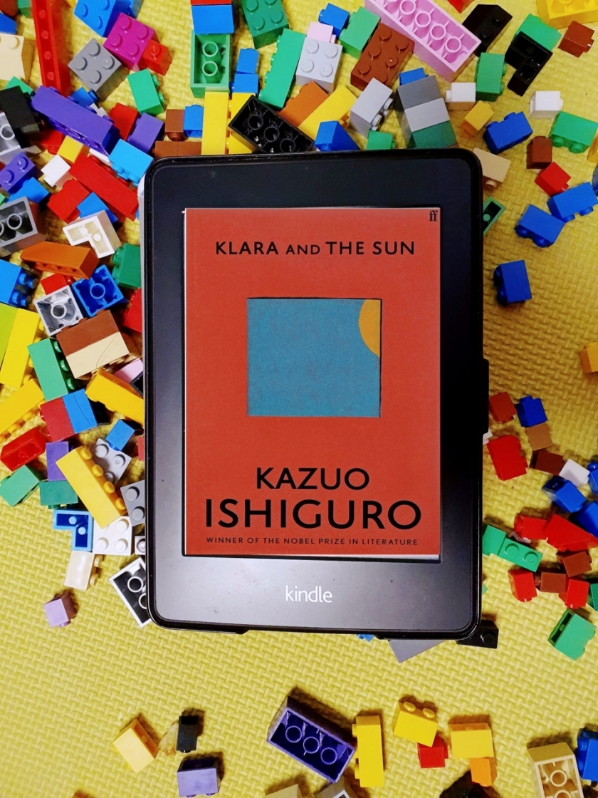 Kindle with the cover of Klara and Sun by Kazuo Ishiguro on a bed of colourful Lego blocks
