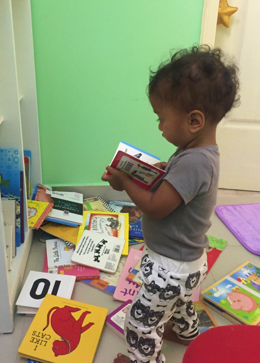 baby reading a book after throwing many books on the floor
