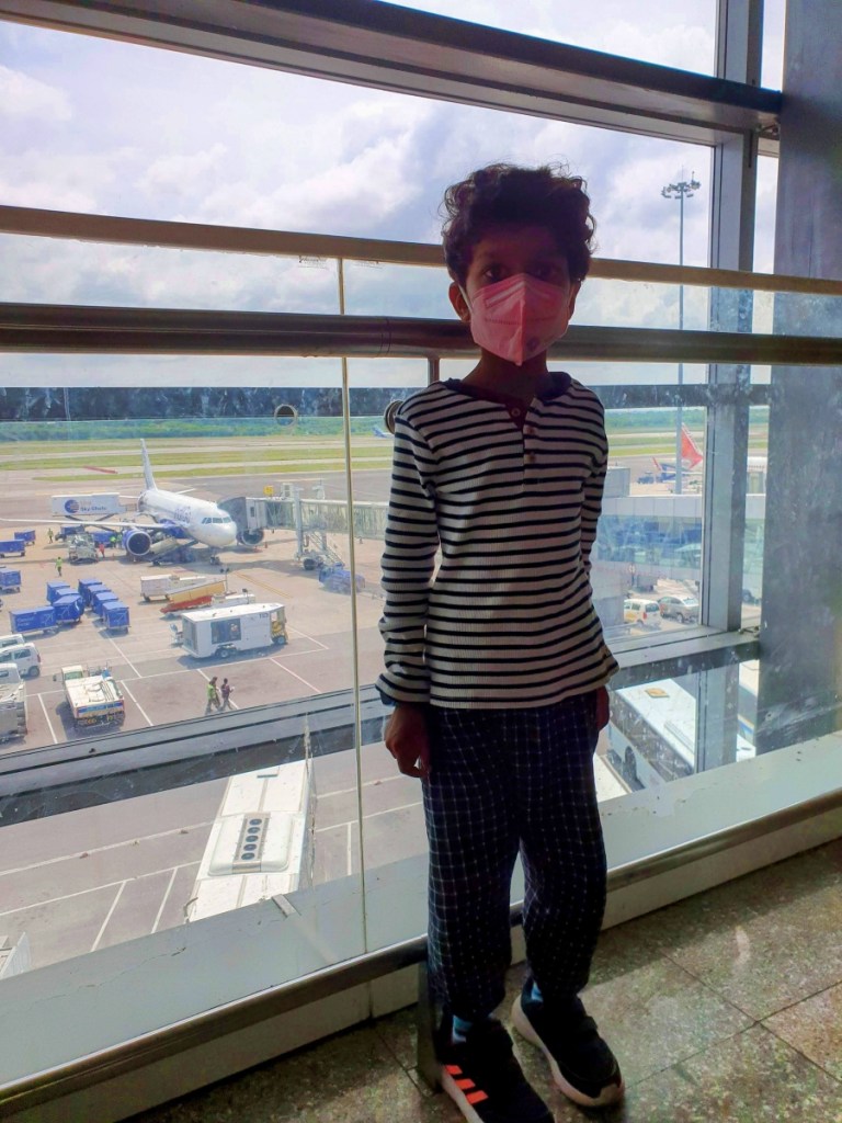 Child in mask standing in the airport with the runway behind him