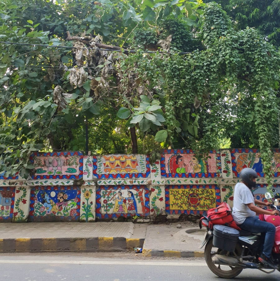 man riding a motorbike in patna with colourful madhubani wall murals behind