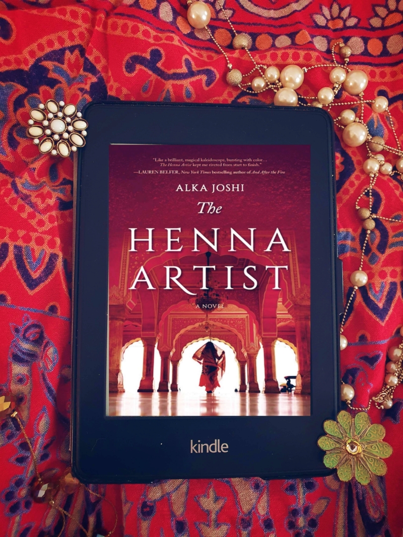 Kindle Paperwhite displaying cover of the henna artist laid on a bright red cloth with jewellery 