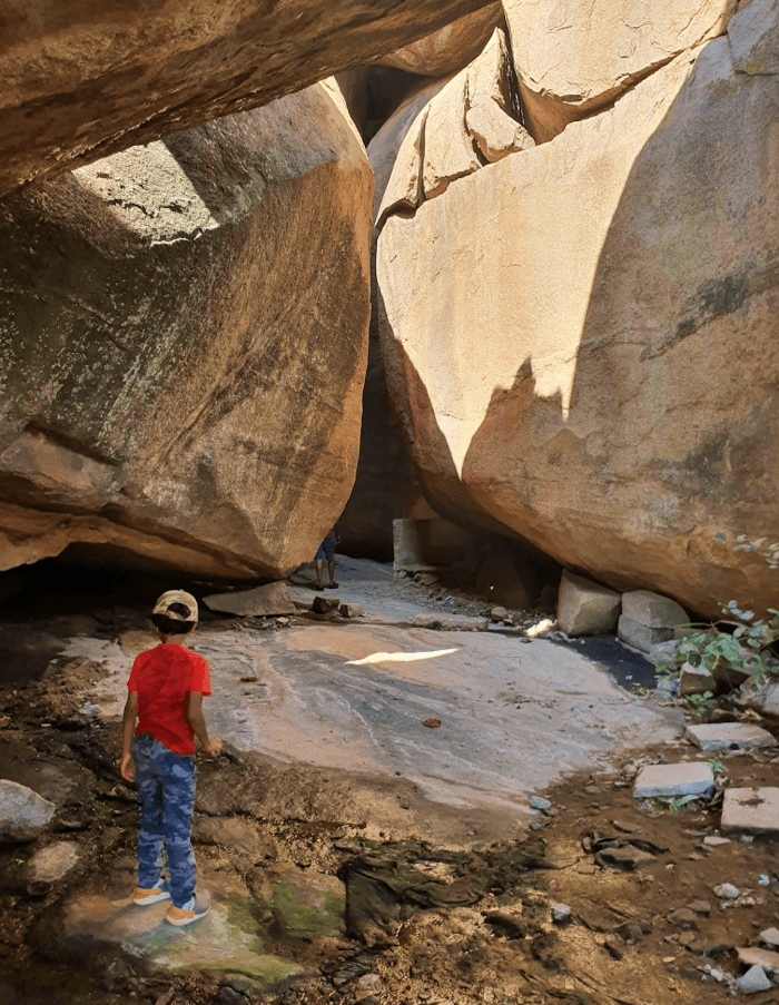 child walking into a small cave between two large boulders in hampi