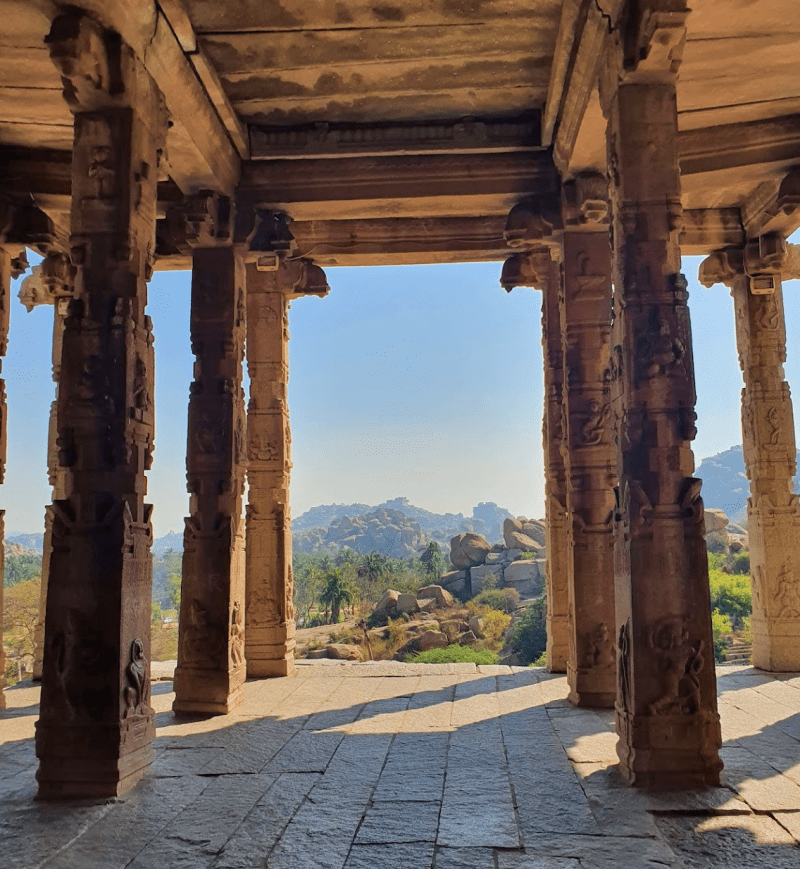 view from the Hampi Kadalekalu Ganesha temple with stone pillars looking out to the view of greenery and mountains