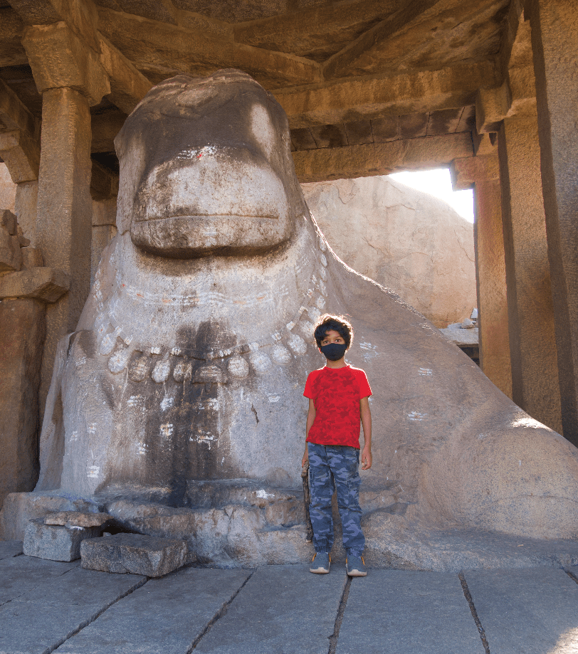 Hampi monolithic Nandi statue with child in mask standing in front of it