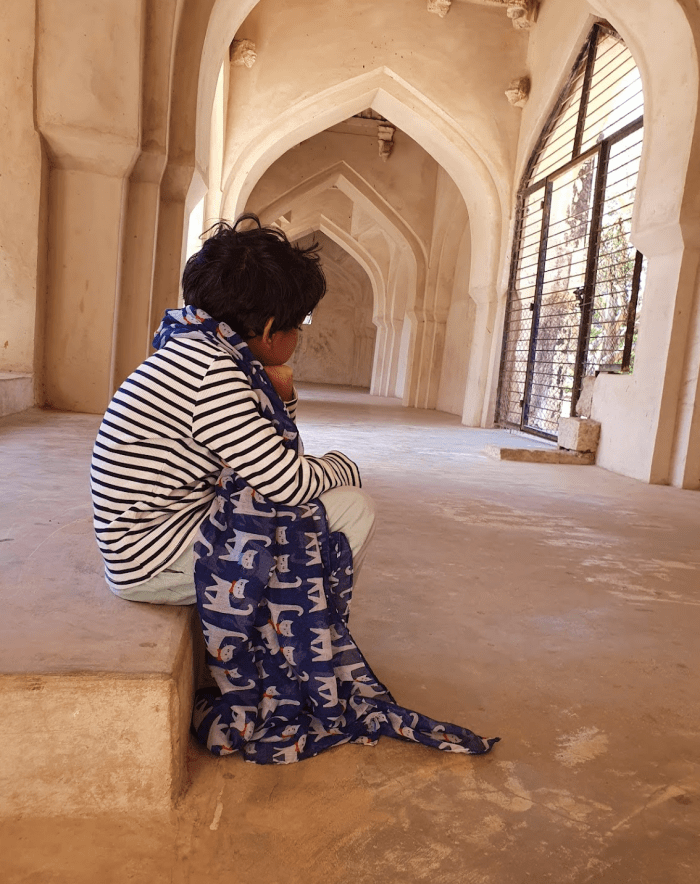 child sitting on a ledge with a scarf getting bored