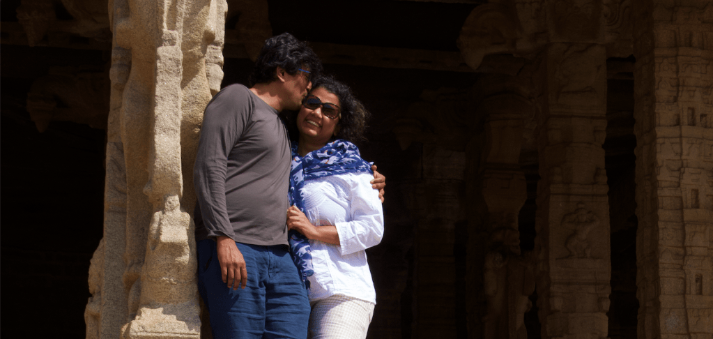 Man leaning against a stone pillar gives his laughing wife a kiss on the cheek