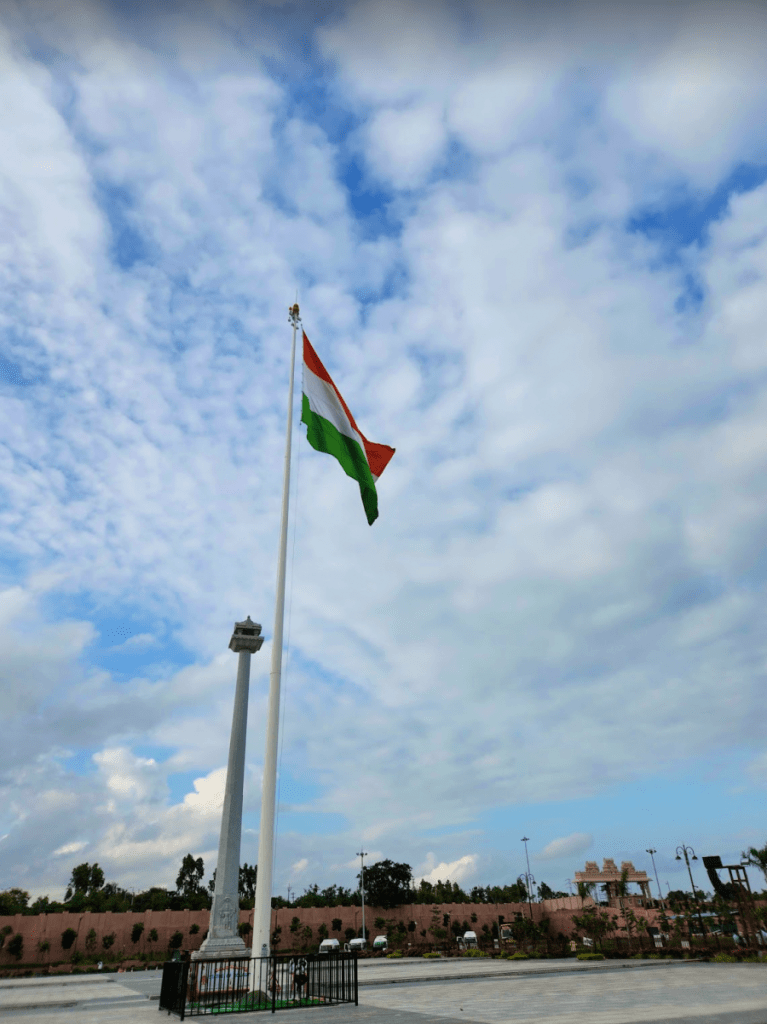 tall India flag in front of the statue of equality in hyderabad, india fluttering on a bright day with blue skies and some white clouds