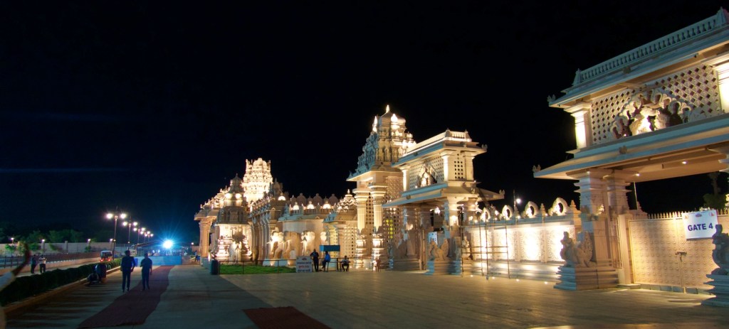 the entrance doors at the statue of equality all lit up at night. the white temple structures shine in the night