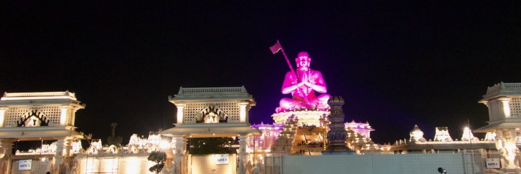 The 216 ft statue of Ramanujacharya lit up in pink light against the dark night sky and surrounding structure in white also lit up: the statue of equality in Hyderabad, India