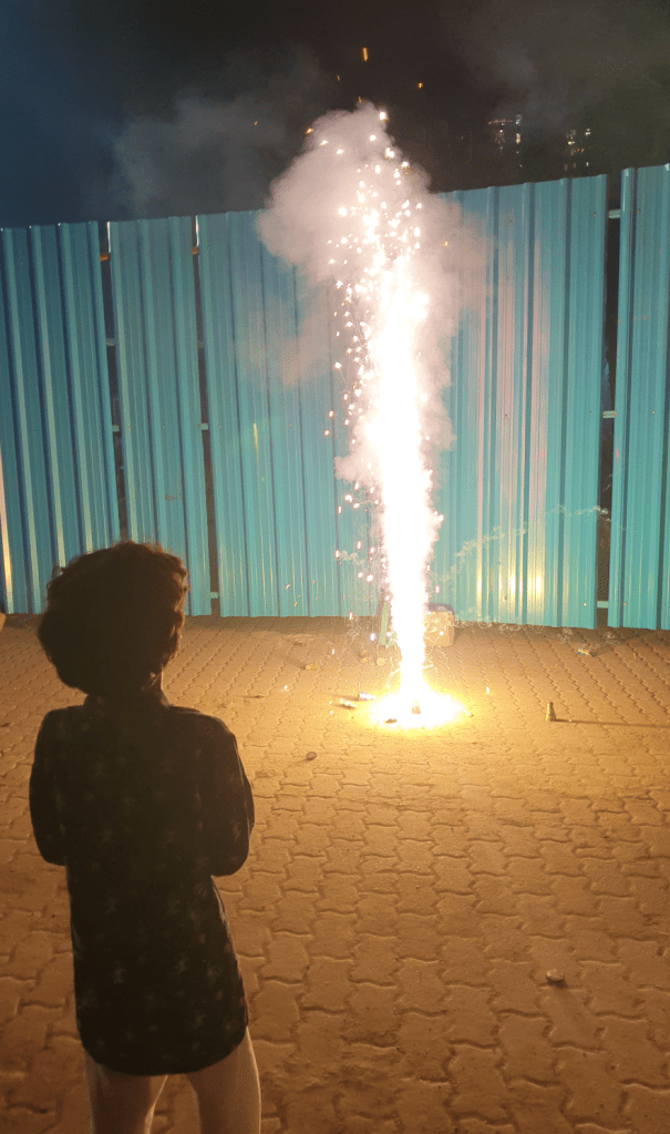 child with his back to the camera in a long shirt looks at a fountain firecracker