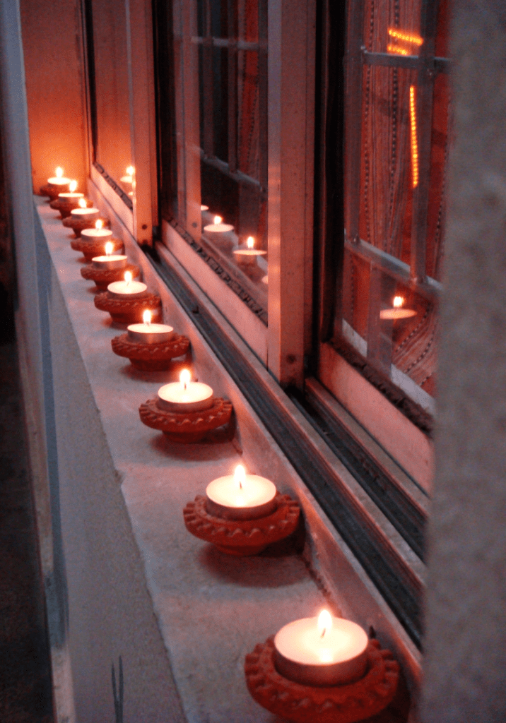 Diwali diyas which is a row of earthen lamps on a windowsill with tealight candles lit inside each of them