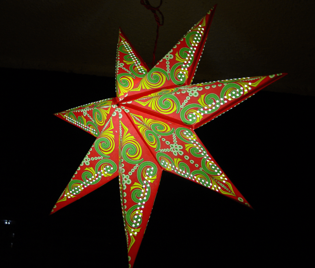 colourful Diwali lantern in the shape of a star with light bulb inside against a dark night sky