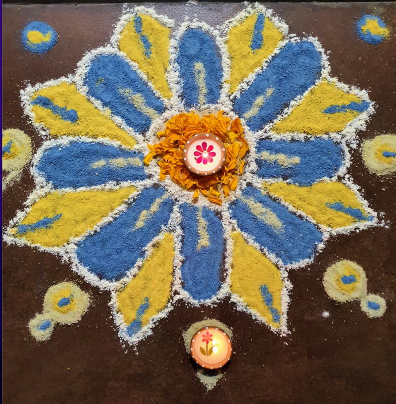 Diwali rangoli in the shape of a flower in blue and yellow made with homemade rangoli colours and some flower petals