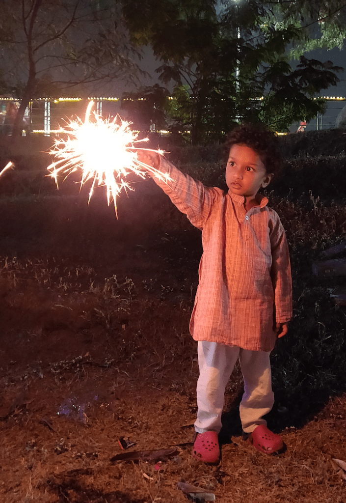 child in kurta pyjama holding a sparkler on Diwali night