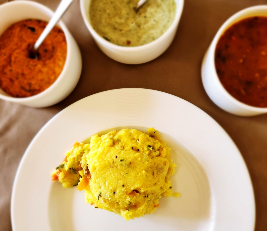 A white plate with a serving of tomato rice. The plate is surrounded by 3 bowls of different chutneys
