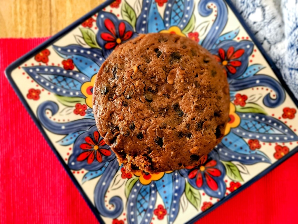 a christmas plum cake set on a colourful square plate with blue, white and red designs. The plate is set on a wooden table top with a red runner