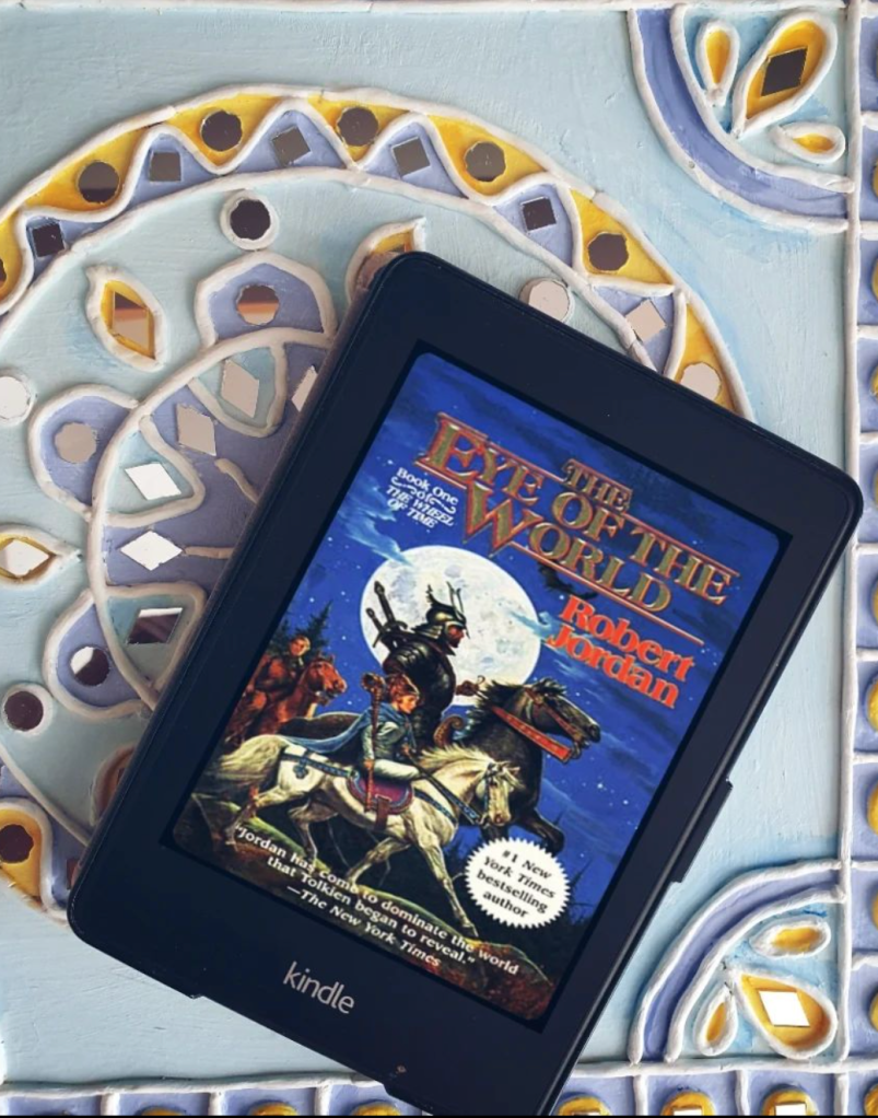 Robert Jordan's Wheel of Time Book 1 The Eye of the World cover on a Kindle Paperwhite set on a blue and purple mirror work art piece