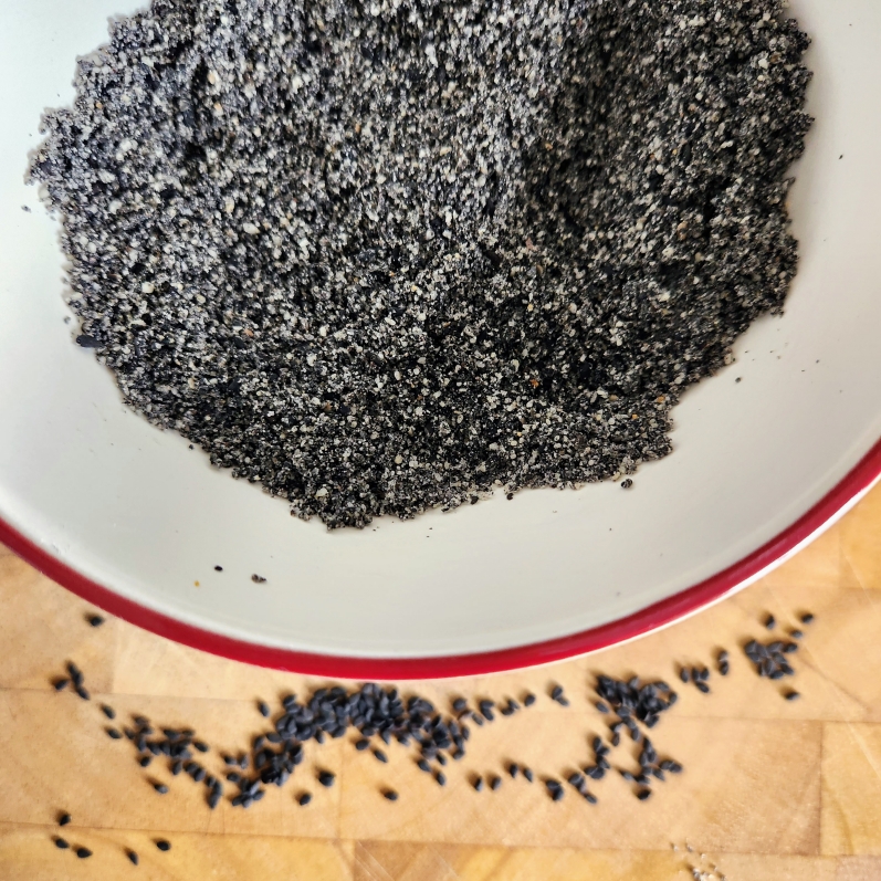 Black sesame seeds in a white bowl with a red rim on a wooden board with some