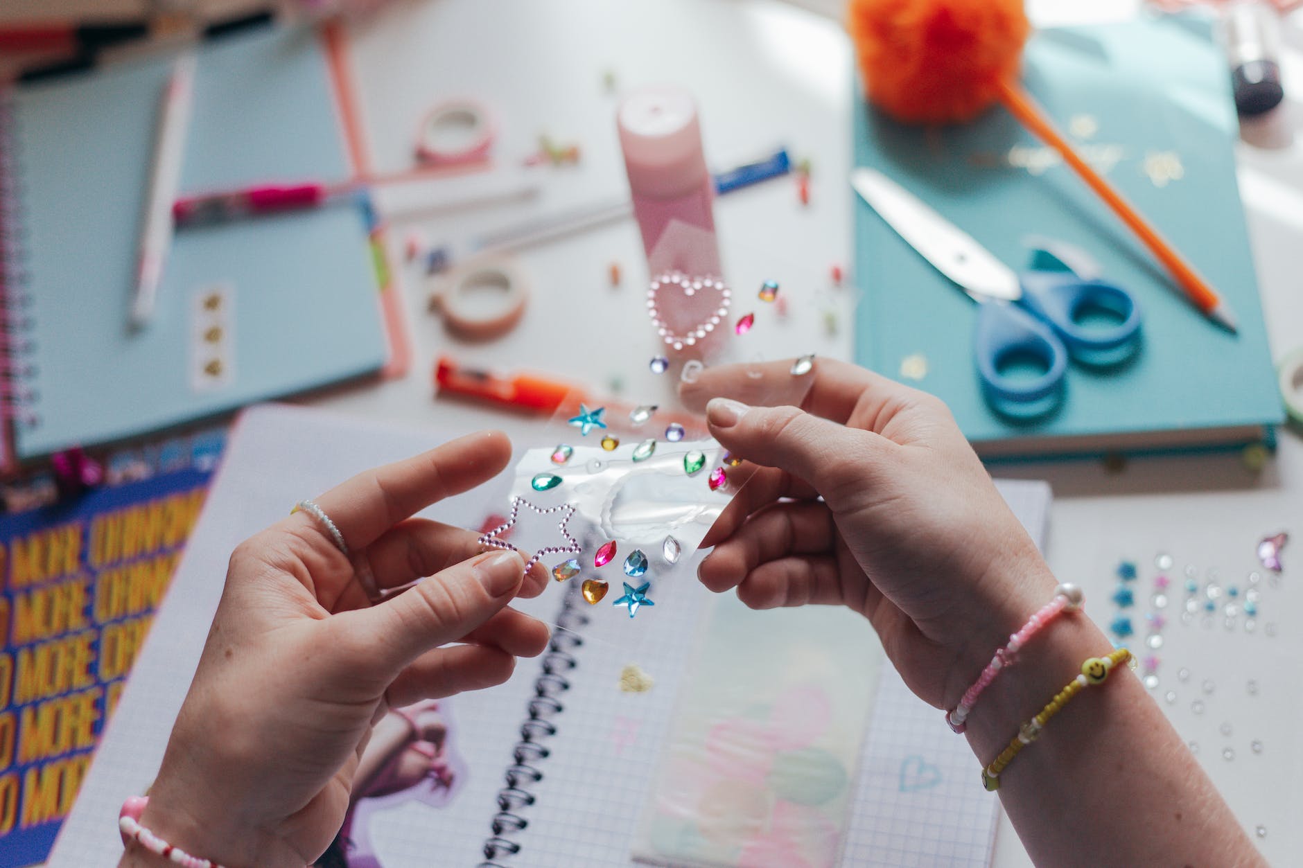 Image of 2 hands holding a sheet of embellishment stickers. In the background are scrapbooking supplies for making a collage