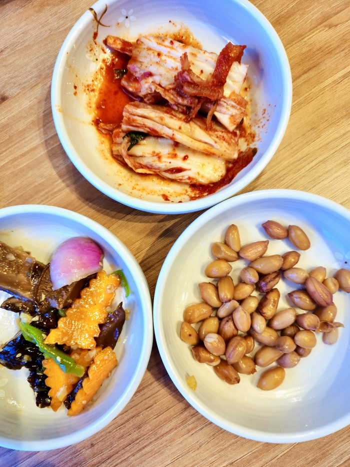 3 plates of korean side dishes called banchan, salad, kimchi and peanuts