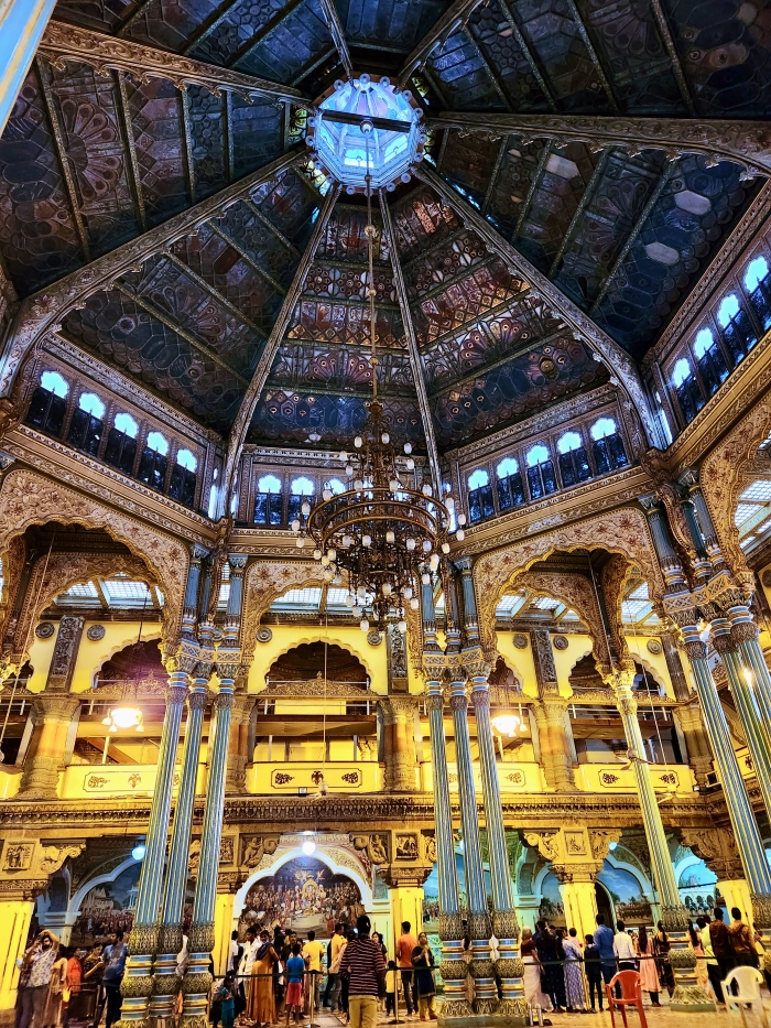 the ornate durbar hall of the mysore palace with high ceilings and a chandelier hanging from it