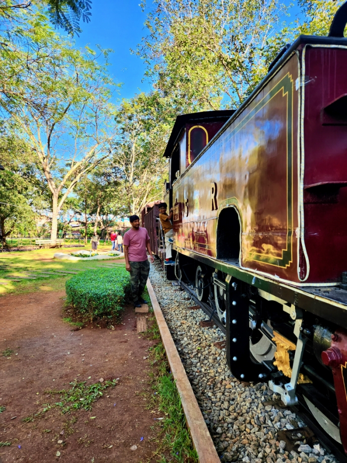 a red train engine kept on a pebbled track for people to explore at the mysuru rail museum in mysore