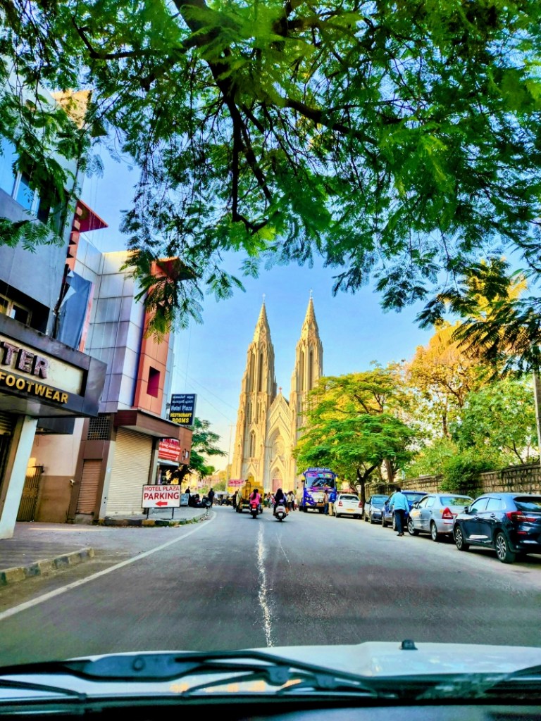 St. Philomena’s Church as seen from the road with cars and shops lined on either side of the road in mysore