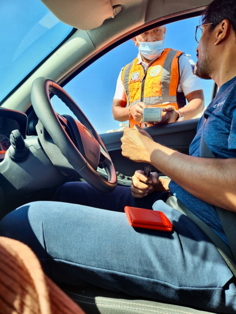 man sitting in the driver's seat of a car, talking to a police officer in an orange vest