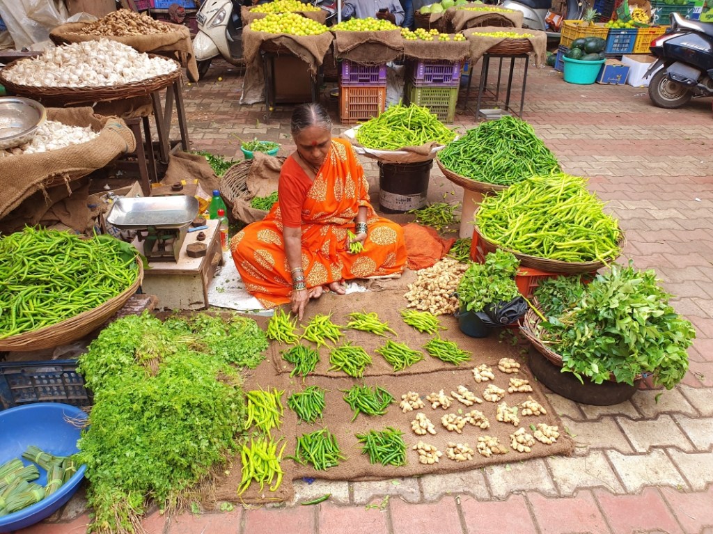 woman in orange sari selling green vegetables
