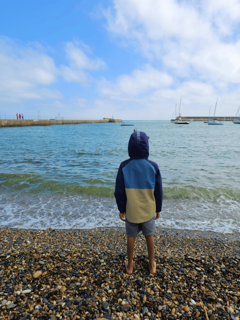 boy in jacket on a pebbled beach looking at the sea in Wicklow, Ireland